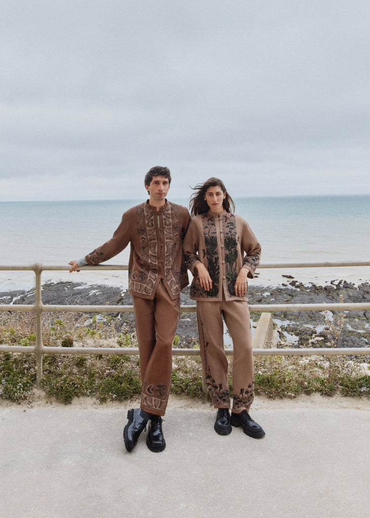 Two people standing on a pathway overlooking a coastal landscape with a cloudy sky.